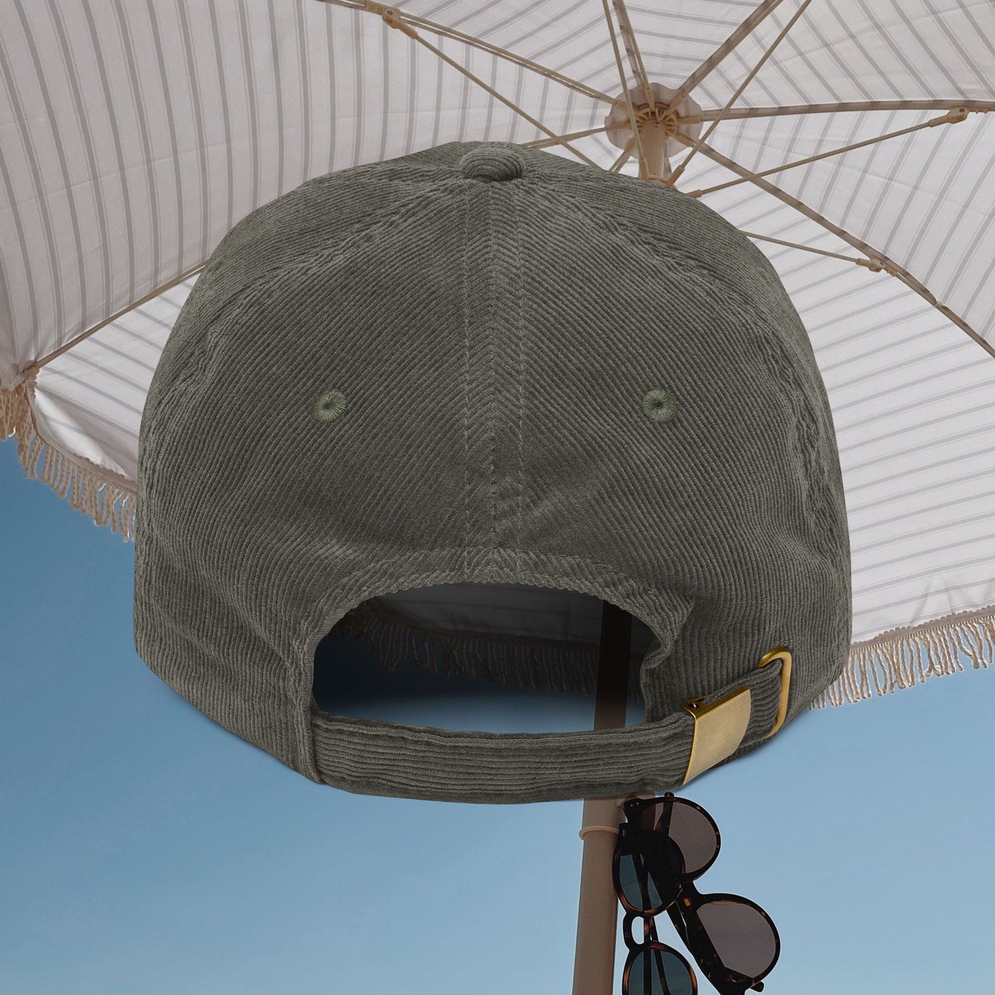 Green cap with a gold buckle on a white umbrella against a blue sky.