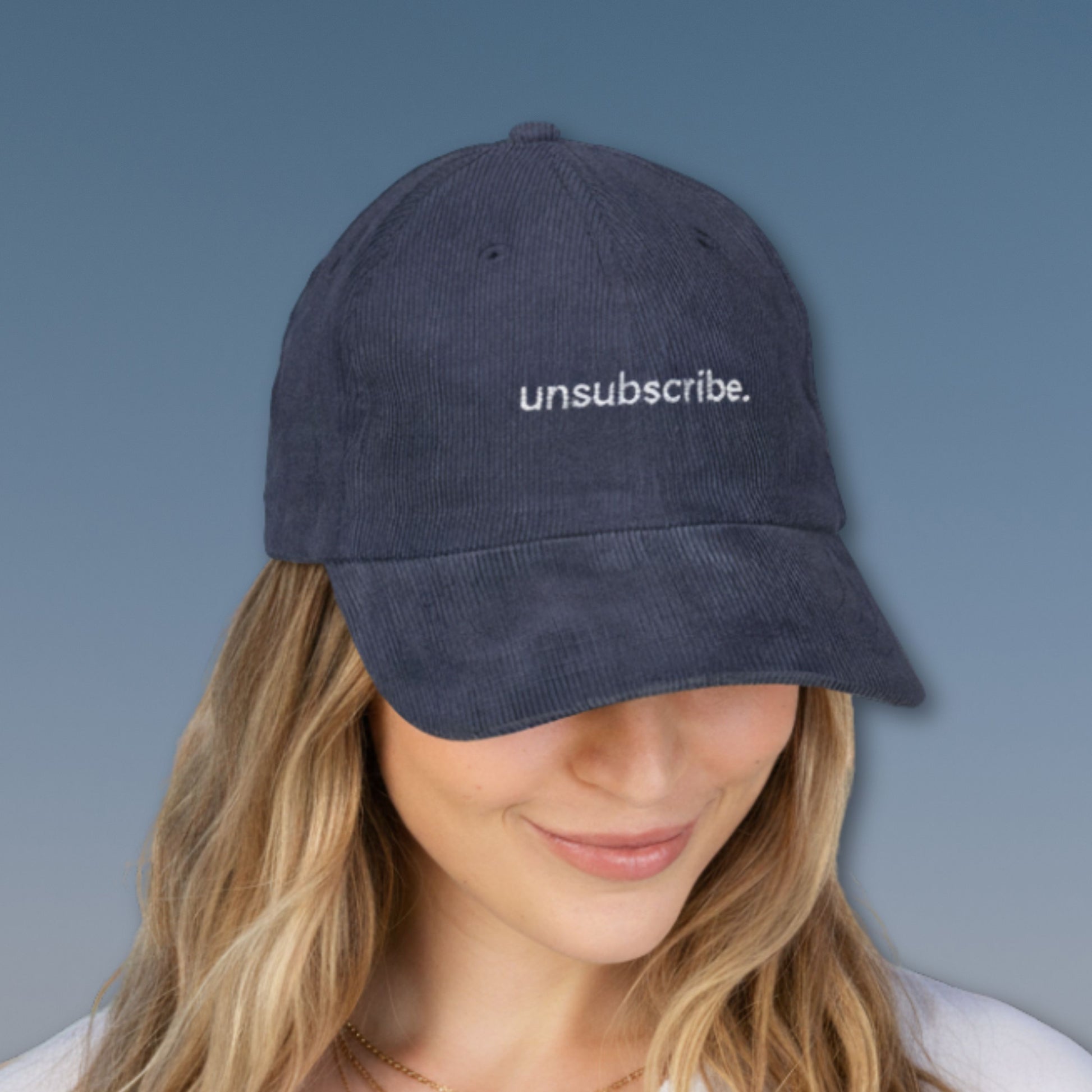 Navy blue cap with 'unsubscribe.' text worn by a person against a blue background