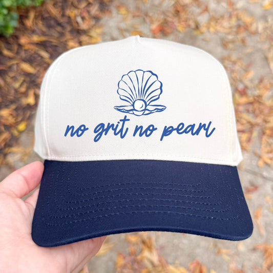 natural and navy cap with 'no grit no pearl' text and shell graphic held by a hand outdoors.